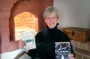 Georgia Piggott in front of her historic bread oven in her Bridport home with her two books Just Causes and Hazardous Game