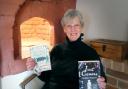 Georgia Piggott in front of her historic bread oven in her Bridport home with her two books Just Causes and Hazardous Game