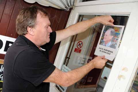 Watch House Cafe staff member Les Spencer placing a Jack Marshall is innocent poster on the entrance door of the cafe 